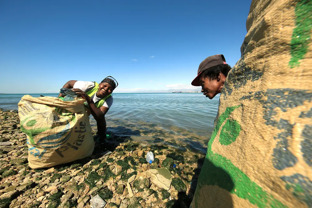 Projeto Plastic Bank: 2 pessoas coletando plástico em uma praia