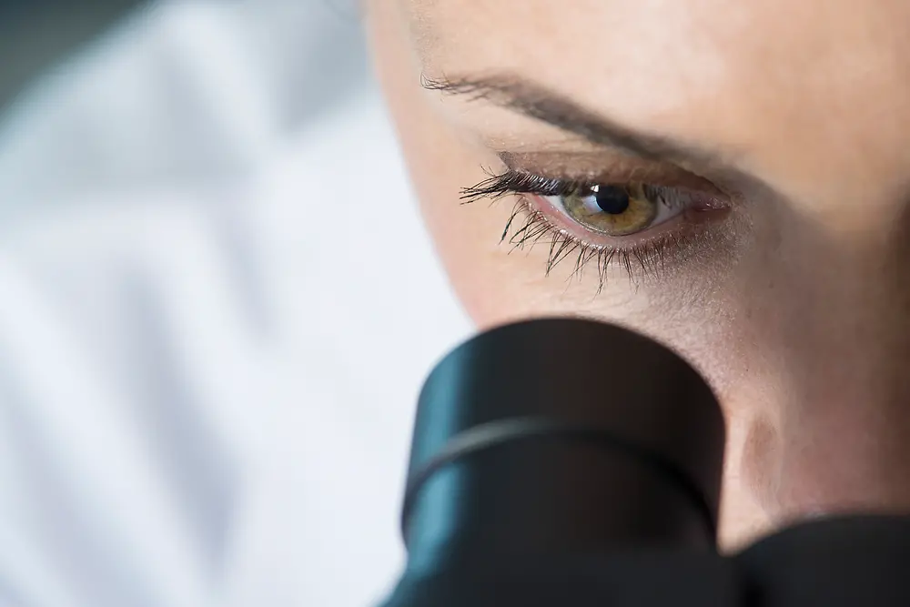 Olho de uma mulher olhando por um microscópio