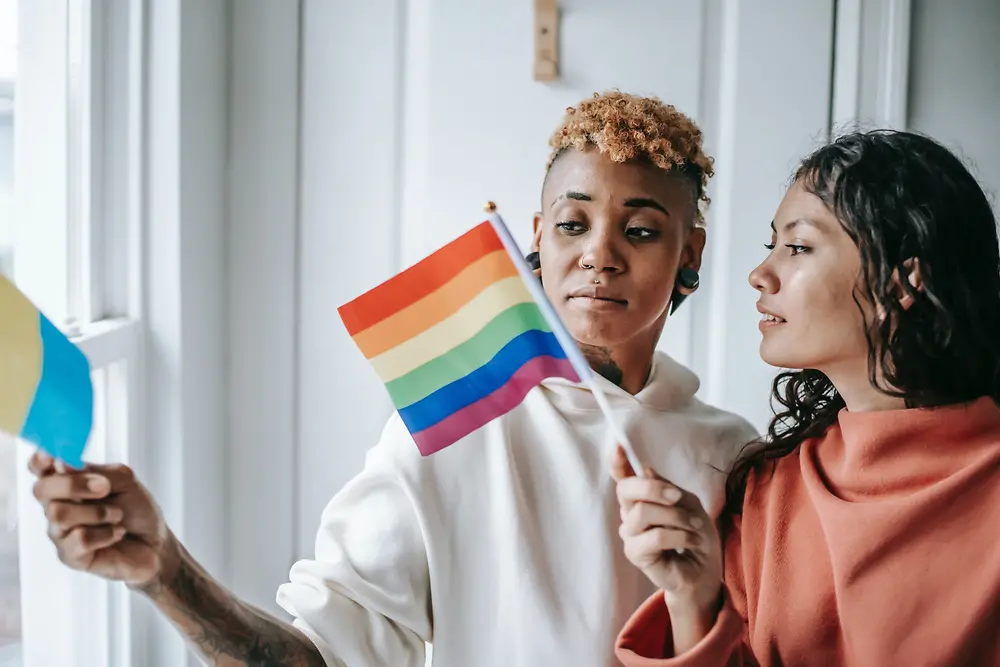Duas mulheres conversam enquanto seguram uma bandeira LGBTQ+.