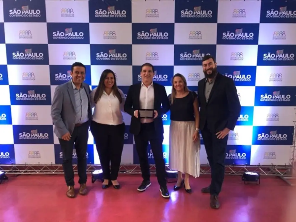Equipe Henkel – cinco pessoas sorrindo. No meio, presidente com o certificado. Atrás, painel com logo do prêmio e do governo