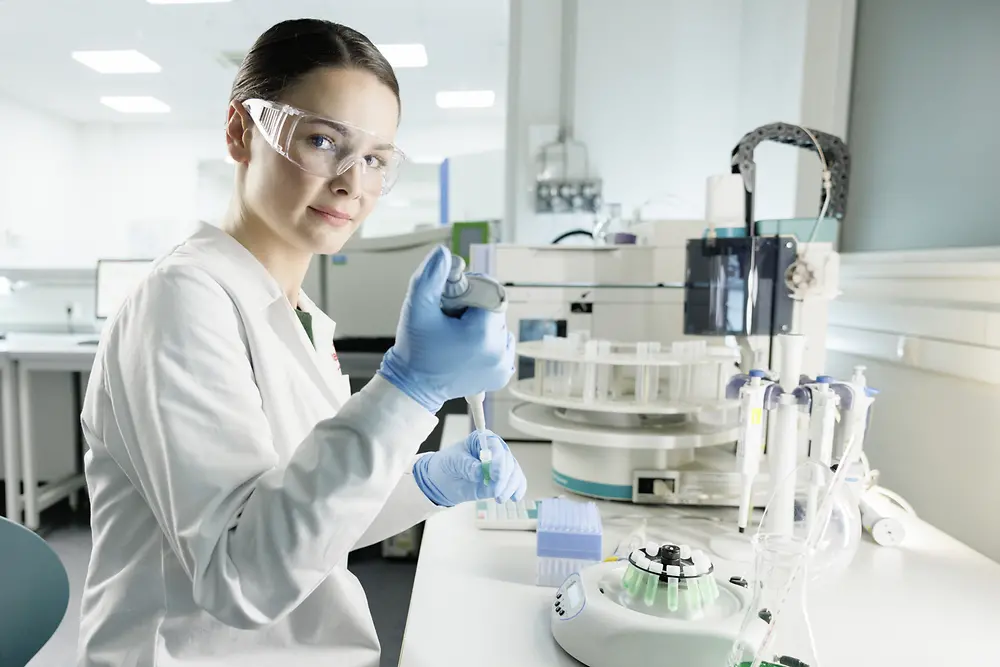 Uma cientista está fazendo experimentos em um laboratório, vestindo um jaleco e óculos de segurança.
