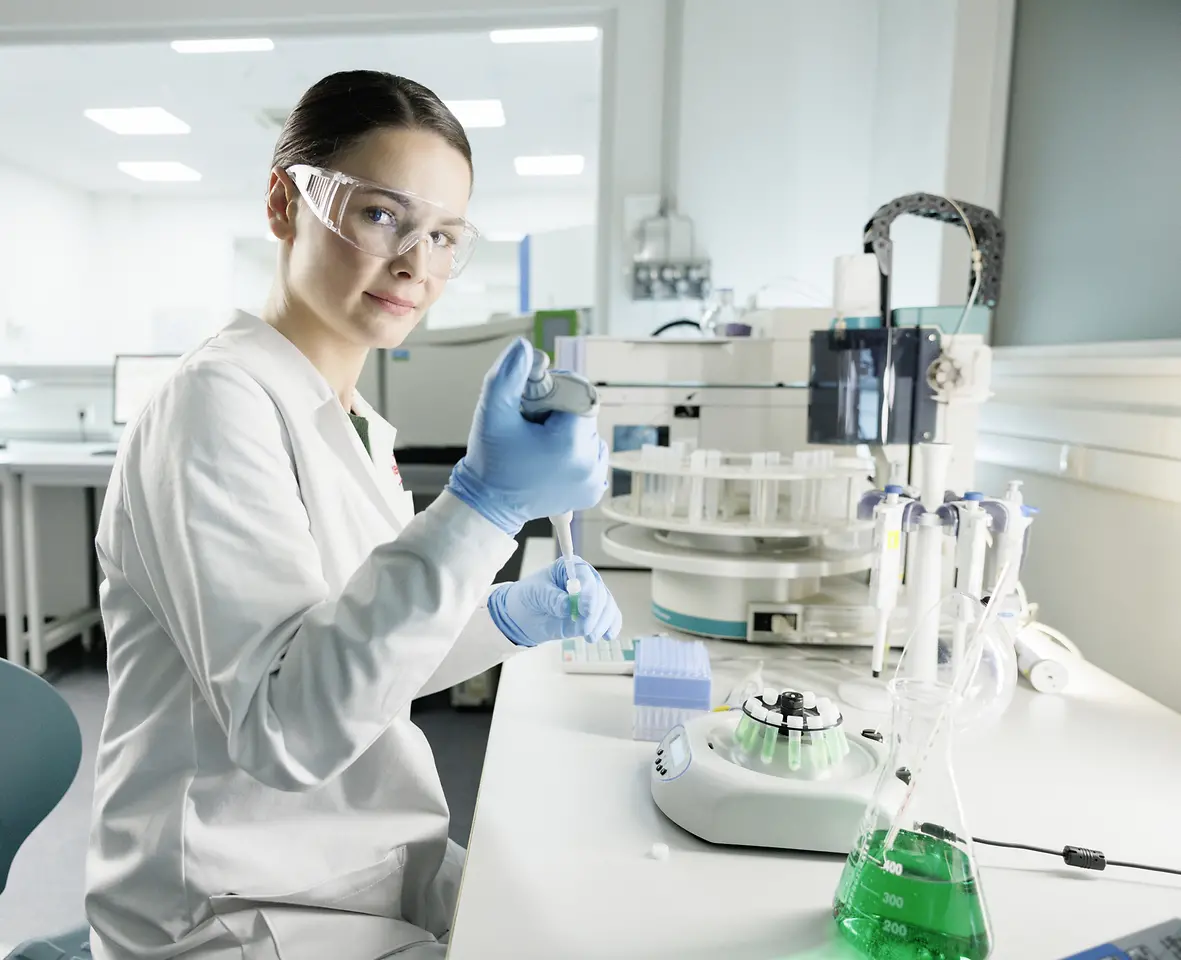 Uma cientista está fazendo experimentos em um laboratório, vestindo um jaleco e óculos de segurança.