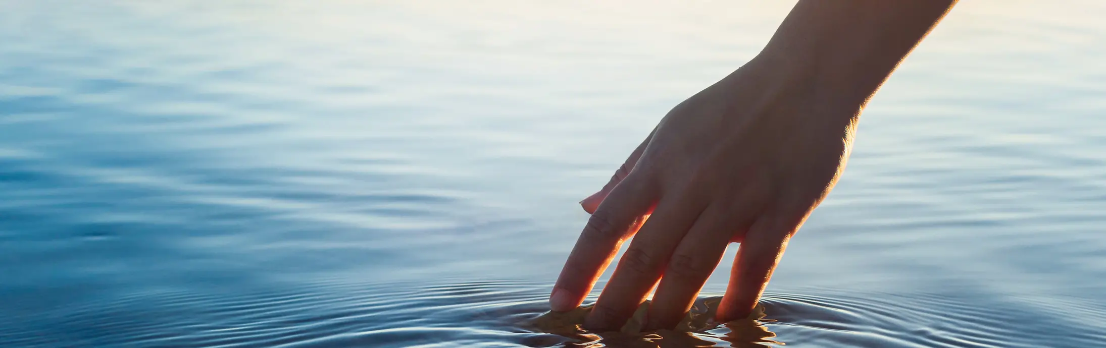 Uma mão acaricia uma superfície de água calma diante do horizonte
