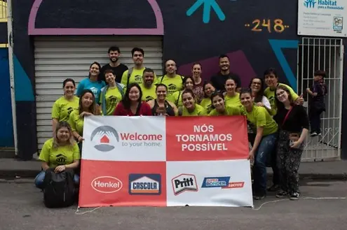 grupo de pessoas segurando uma faixa com o logo da Henkel e das marcas Pritt, Super Bonder e Cascola