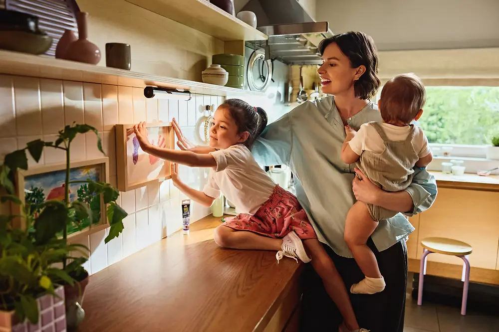 A mother and her daughters hang a picture on the wall using Pattex Stick and Peel.