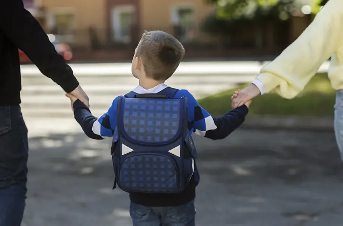 Pais segurando as mãos de uma criança indo para a escola