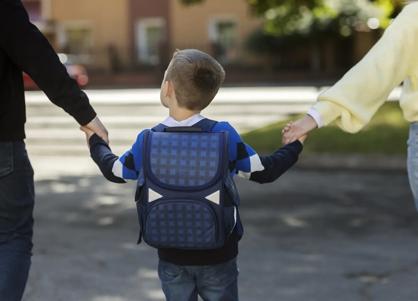 Pais segurando as mãos de uma criança indo para a escola