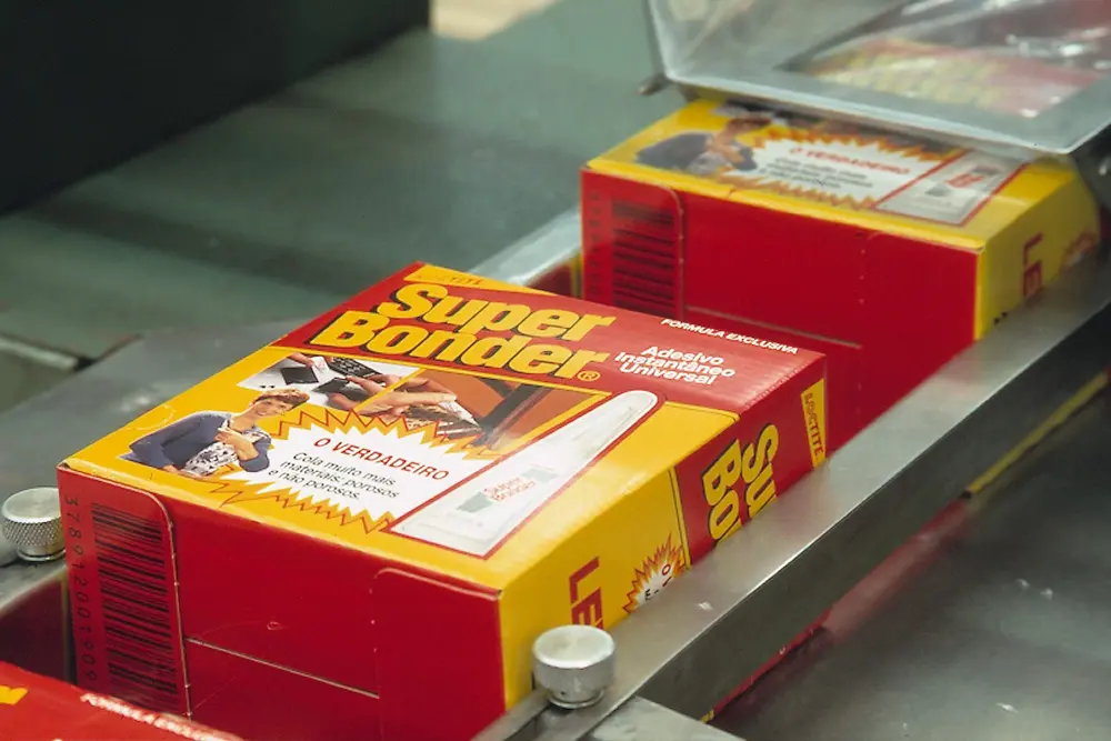 Caixas antigas de Loctite Super Bonder, trazendo ilustrações da marca (1997) em vermelho e amarelo, na linha de produção.