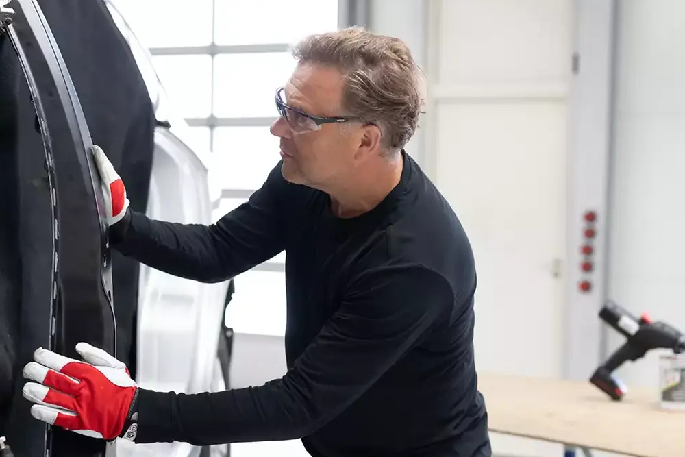 Técnico reparando ou fazendo manutenção na porta de um veículo em uma oficina mecânica.