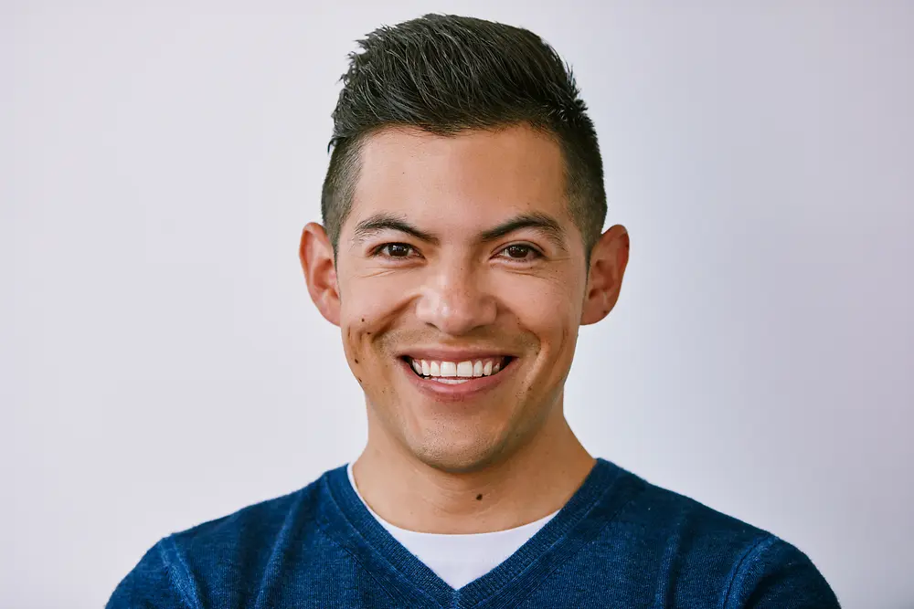 Retrato profissional de uma pessoa vestindo um suéter azul diante de um fundo claro.