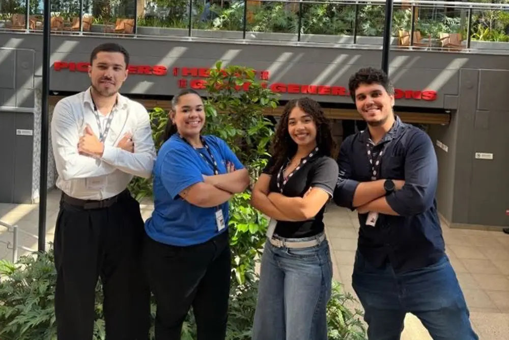 Quatro estagiários em frente ao prédio do Centro de Inovação, sorrindo e posando com os braços cruzados.